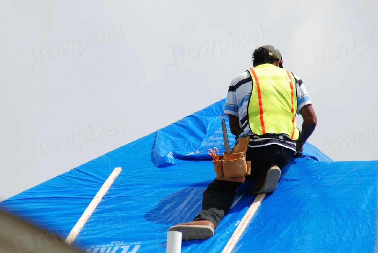 Roofers installing an emergency roof tarp after storm damage