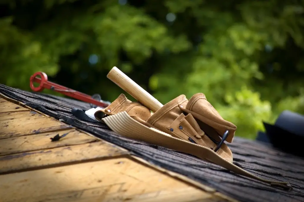 Roofer with tool belt installing asphalt shingles